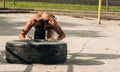 Strong sporty guy flipping workout wheel at outside gym