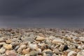 Strong storm is approaching from the sea on the shingle beach. Dark storm clouds and sunlit pebbles.