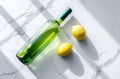 Strong sunlight casts shadows on a white marble surface, where a green bottle and fresh lemons are arranged, creating a scene that Royalty Free Stock Photo