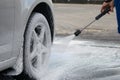 Strong water pressure washes off a thick foam from the wheels of the car