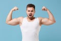 Strong young bearded guy 20s in white singlet posing isolated on pastel blue wall background studio portrait. Sport