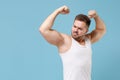 Strong young bearded guy 20s in white singlet posing isolated on pastel blue wall background studio portrait. Sport