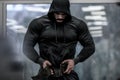 Strong young bearded mighty man in hoodie wearing powerlifting belt for heavy hardcore weight training workout indoors sport