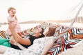 Strong young father holding his baby daughter in hands with happy hipster mother, smiling family relaxing in a hammock on a beach Royalty Free Stock Photo