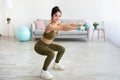 Strong young Indian woman working out with dumbbells, squatting at home, empty space Royalty Free Stock Photo