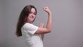 Strong young lady in white shirt showing muscules, looking at camera