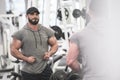 Strong young caucasian man with beard looking at his big muslces before mirror in sport gym