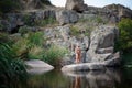 A strong young man sits on a rock in the middle of the water in summer. Summer swimming in the river among rocks. Royalty Free Stock Photo