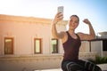 Strong young sporty woman with phone showing her muscles outdoors Royalty Free Stock Photo