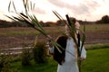 Strong young woman with a bulrush grass reed on rural field background at sunset