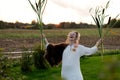 Strong young woman with a bulrush grass reed on rural field background at sunset