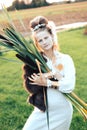 Strong young woman with a bulrush grass reed on rural field background at sunset