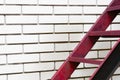Part of the stairs red metal ladder leading up against of a white brick wall Royalty Free Stock Photo