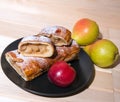 Strudel with apples on a black and white plate with yellow pears, peaches