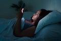 Struggling with sleeplessness woman, ensnared in bed& x27;s embrace, gazes at her phone& x27;s radiant screen