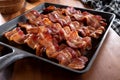 crispy strips of bacon in a black in a square cast iron pan on a wood cutting board Royalty Free Stock Photo