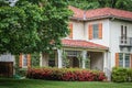 Stucco House with orange shutters and tile roof and porch with trellis and azeleas bushes in bloom with large trees in spring