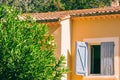 Stucco structure with an open window and blue paint peeling shutters