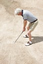 Stuck in the sand trap. Senior man trying to hit his ball out of the sandtrap on the golf course. Royalty Free Stock Photo