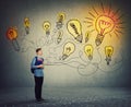 Student boy holding books and backpack imagining bright lightbulbs on the wall. Smart and ingenious teen guy has different