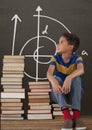 Student boy on a table looking up against grey blackboard with school and education graphic