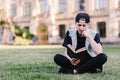 A student carefully reads a book sitting on a grass in a park near a college. Teenager reading a book outdoors Royalty Free Stock Photo