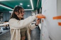 Student woman pins orange sticky notes on wall during classroom planning session Royalty Free Stock Photo