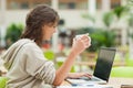 Student drinking coffee while using laptop at cafeteria table