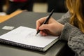Student engages in note-taking with pen on a grid notebook during a classroom session Royalty Free Stock Photo