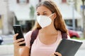 Student female with protective mask reading a message on smart phone in the street