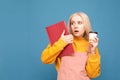 Student funny girl stands with a notepad and a cup coffee in her hands,looks aside,blue background.Surprised teenage girl holds a