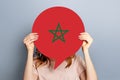 student girl holds blank white speech bubble with the flag of Morocco isolated over grey studio background