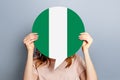 student girl holds blank white speech bubble with Nigeria flag isolated over grey studio background