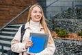 Student girl holds folders notebooks books in hands smiles, looks away against the background of a modern university Royalty Free Stock Photo