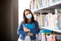 Student girl in mask with book at library Royalty Free Stock Photo