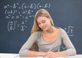 Student girl at table writing against blue blackboard with education and school graphics Royalty Free Stock Photo