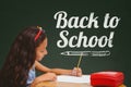 Student girl at table writing against green blackboard with back to school text Royalty Free Stock Photo