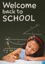 Student girl at table writing against green blackboard with welcome to school text Royalty Free Stock Photo