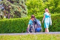 a student girl walks with her friend to the disabled sitting in a wheelchair along the Volga River embankment on a sunny summer d