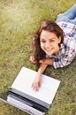 Top view if student girl working on laptop, lying on grass in park