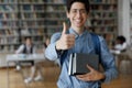 Student guy posing in library showing thumbs up at camera