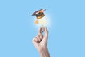 Student hand holding light bulb with graduation hat on blue Royalty Free Stock Photo