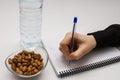 Student hand holding pen and writing notes in the notebook and glass bowl of hazelnuts and water bottle isolated Royalty Free Stock Photo