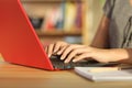 Student hands writing in a red laptop at home