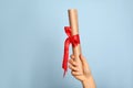 Student holding rolled diploma with red ribbon on light blue background, closeup Royalty Free Stock Photo