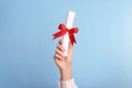 Student holding rolled diploma with red ribbon on light blue background, closeup Royalty Free Stock Photo