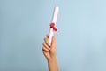 Student holding rolled diploma with red ribbon on light blue background, closeup Royalty Free Stock Photo