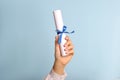 Student holding rolled diploma with ribbon on light blue background, closeup Royalty Free Stock Photo