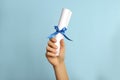 Student holding rolled diploma with ribbon on light blue background, closeup Royalty Free Stock Photo