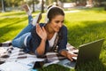 Student lies outdoors in a park using laptop computer listening music waving. Royalty Free Stock Photo